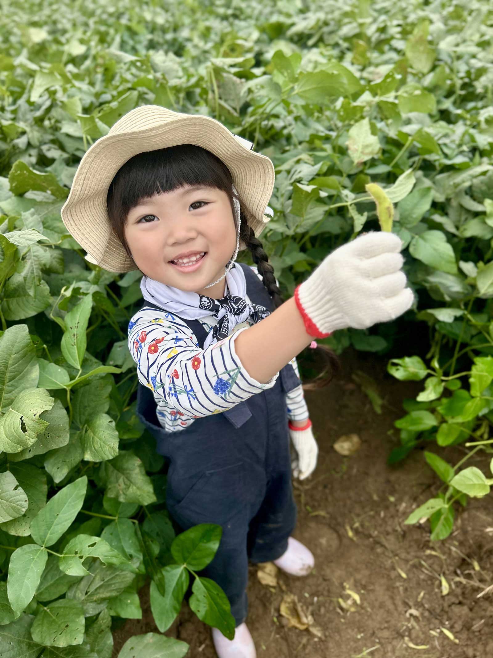 畑で収穫した枝豆を笑顔で見せる子ども